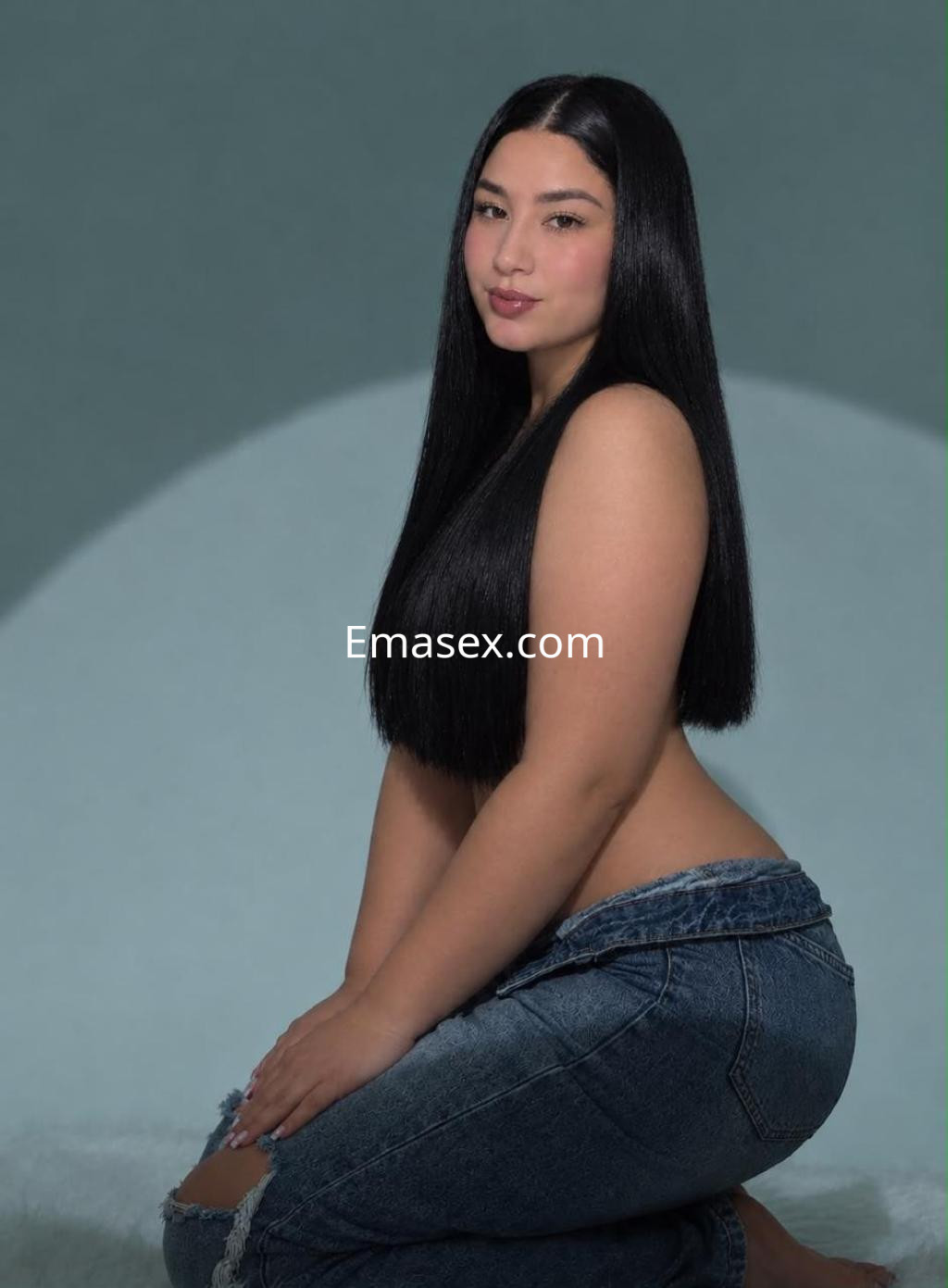 La escort en Vitoria muestra su cabello largo y lacio, posando con un jeans de tiro bajo en un fondo suave.