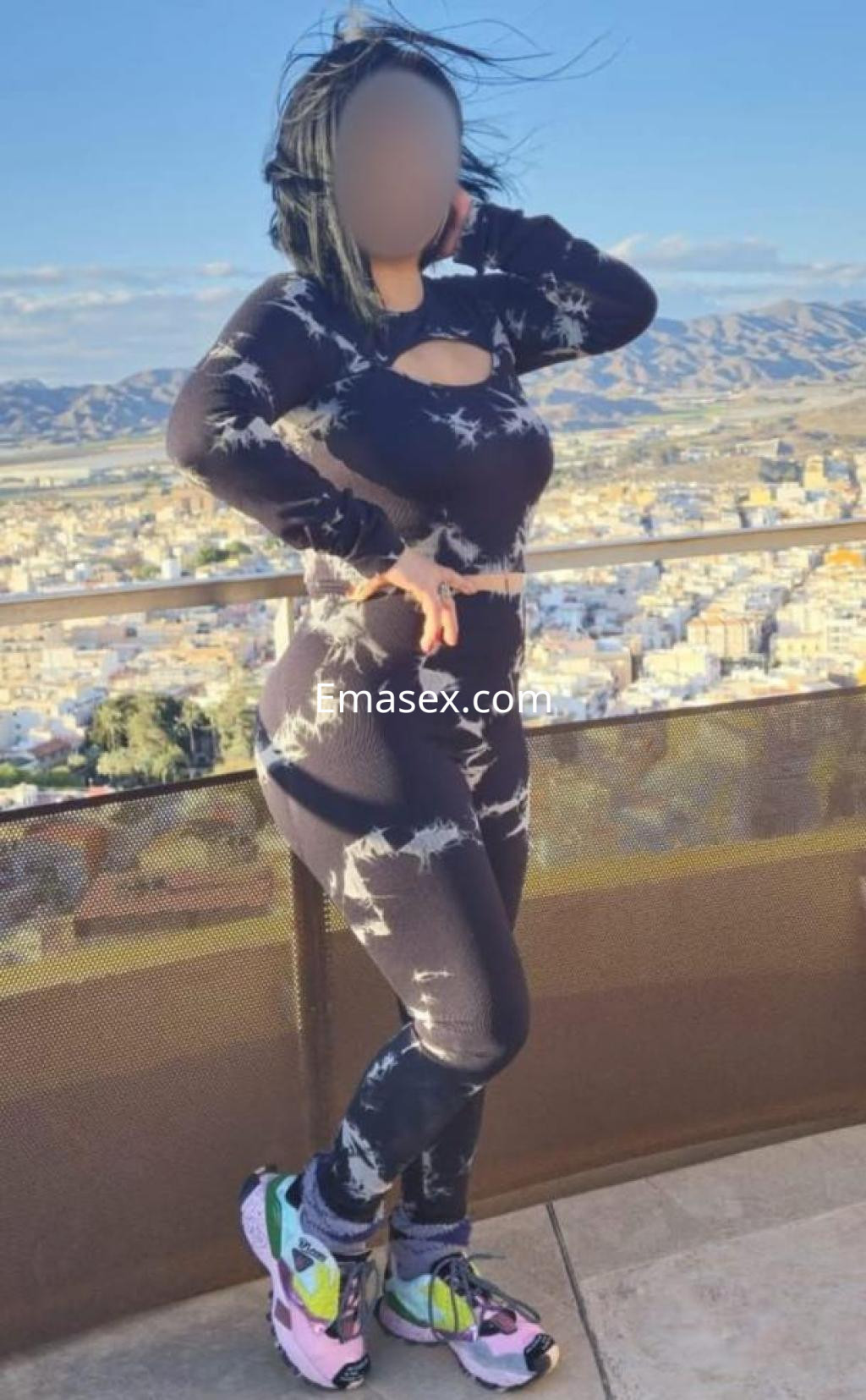 Escort posando al aire libre en Murcia, con un conjunto ajustado de tonos oscuros y zapatillas de colores.