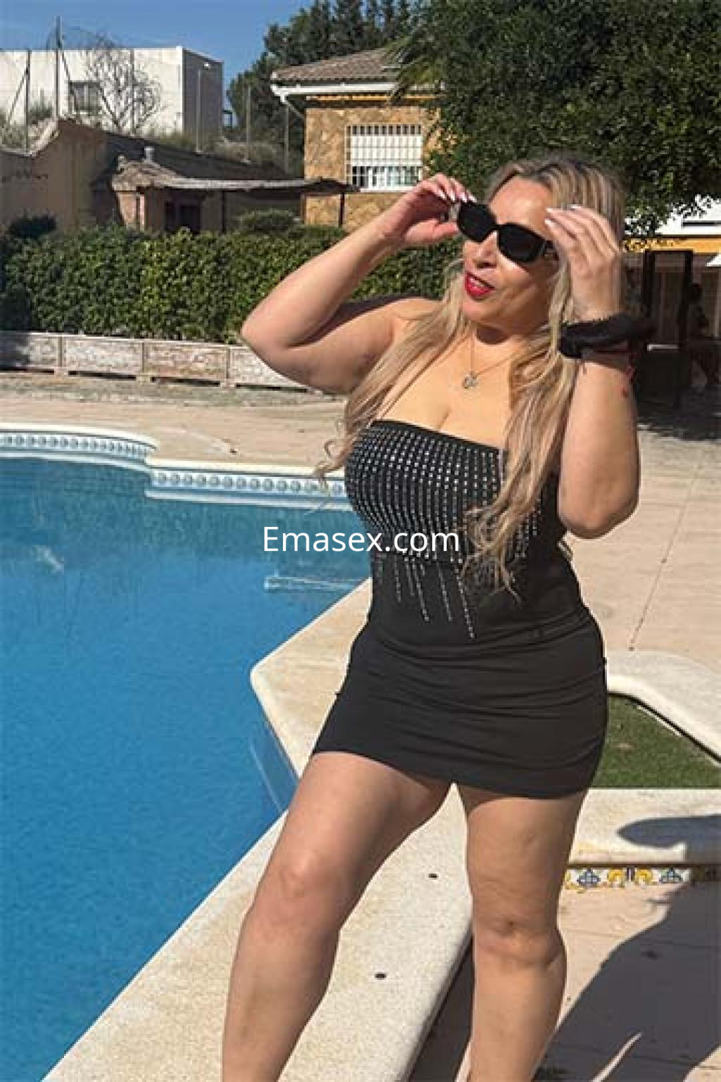 Escort en Logroño luciendo un vestido negro ajustado y gafas de sol, posando junto a una piscina.