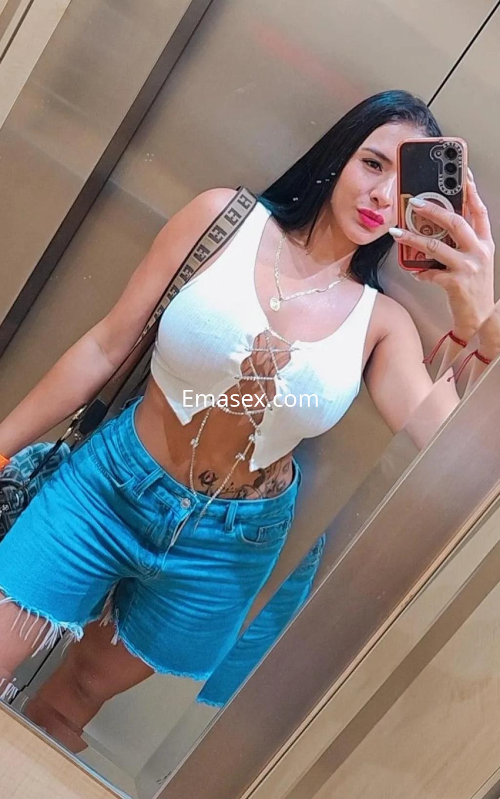 Puta en Coruña, posando frente a un espejo en un top blanco y shorts de mezclilla, con cabello largo y lacio.
