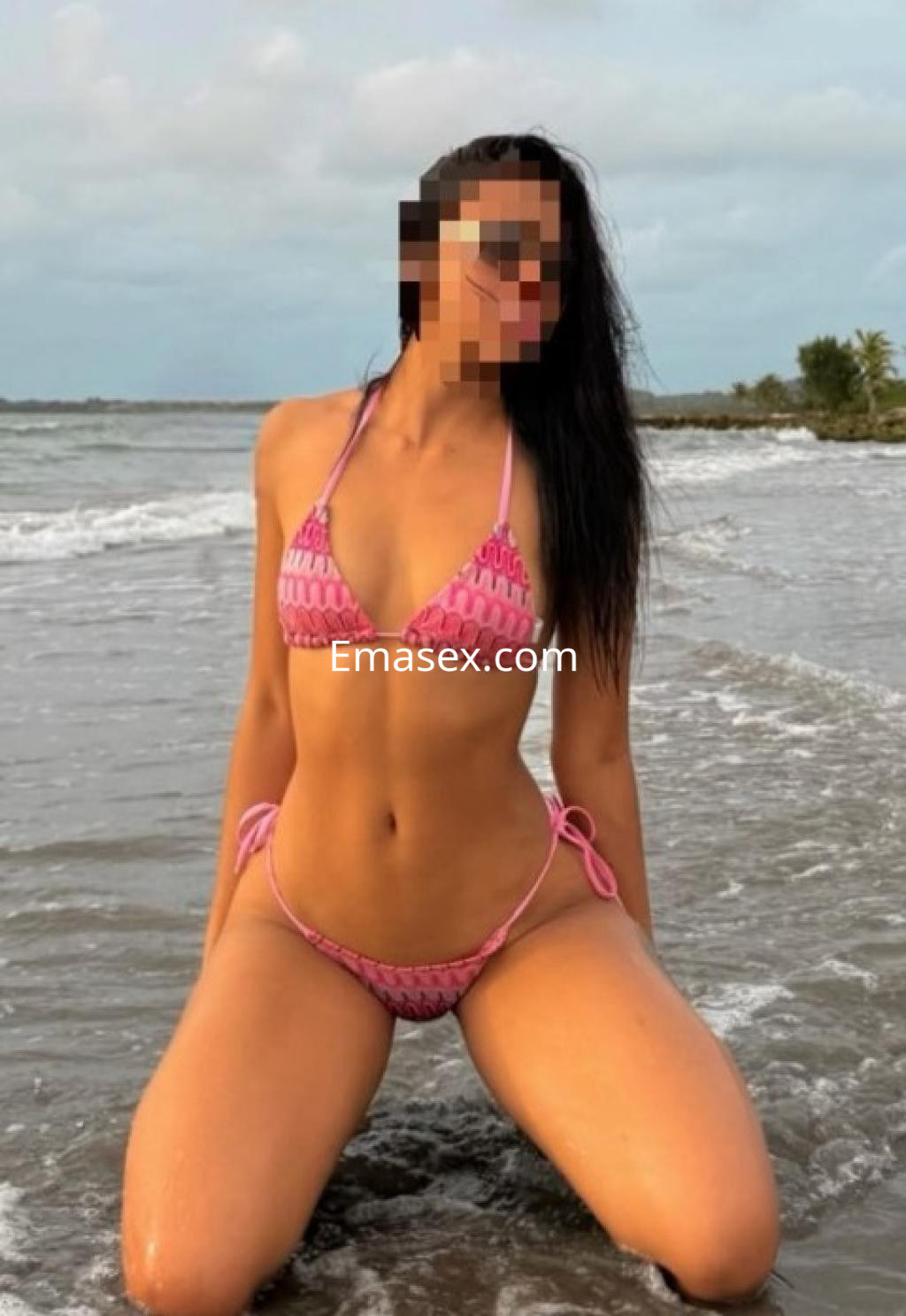 Puta en Lleida, de rodillas en la playa con un bikini rosa, cabello largo y oscuro, disfrutando del mar.