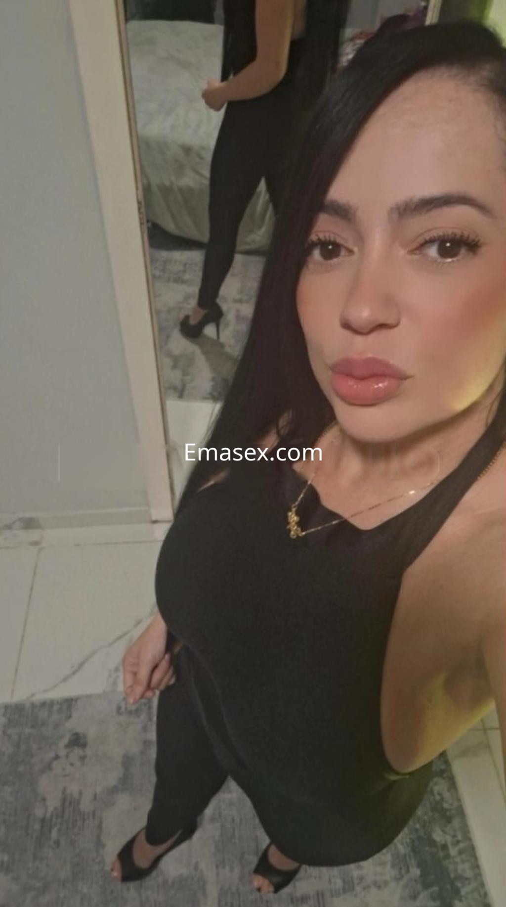 Puta en Lleida, posando frente al espejo con un atuendo negro ajustado y cabello largo, luciendo sensual.