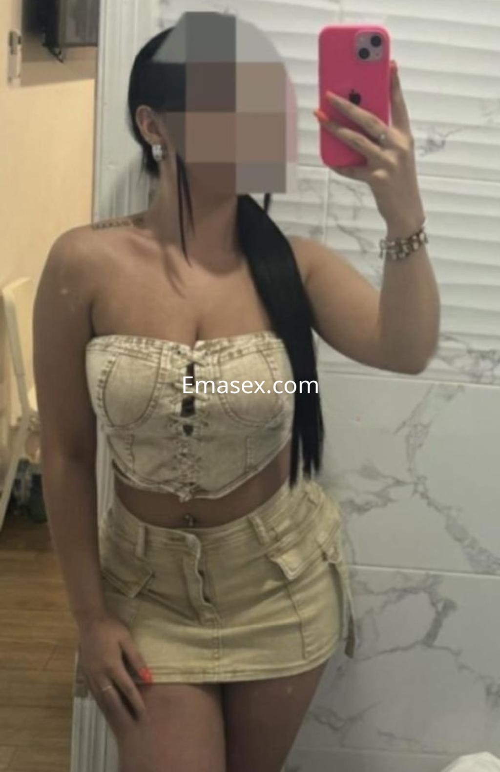 La escort posa en un espejo, vistiendo un top de mezclilla strapless y una falda corta en un ambiente de Málaga.