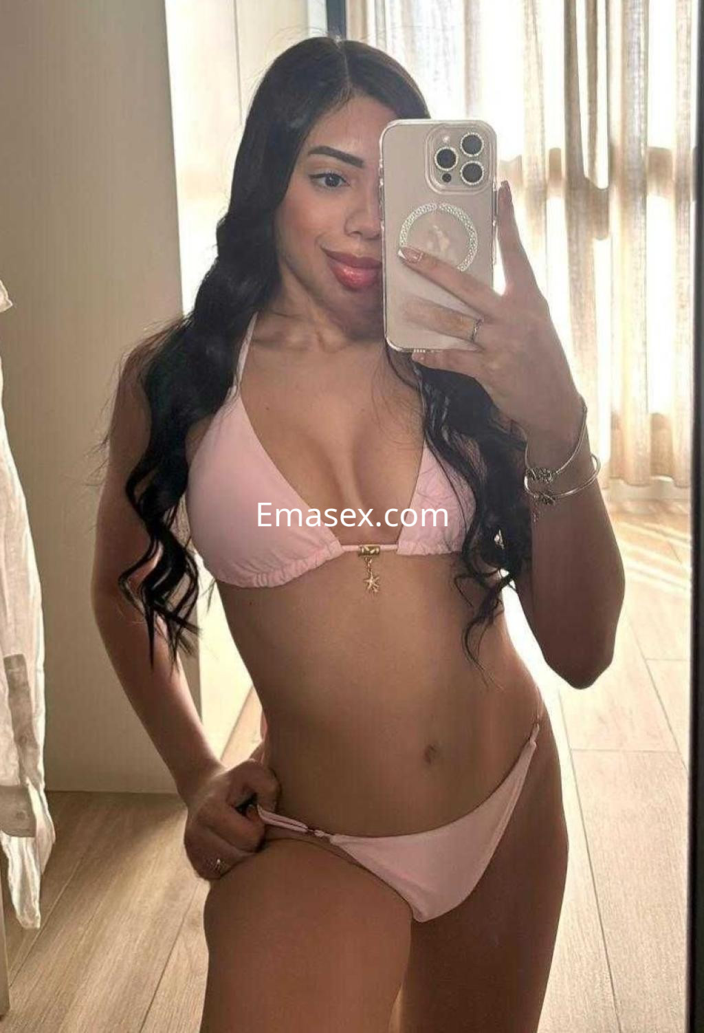 Escort en Málaga posa frente al espejo, luciendo un bikini rosa y con cabello largo y ondulado.