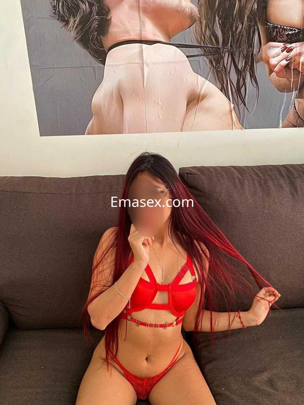 Escort en Pontevedra con cabello largo y rojo, vistiendo un conjunto de lencería roja, sentada en un sofá.