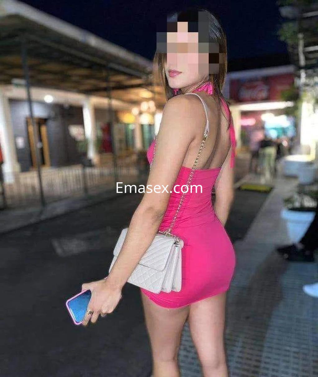 Puta con vestido rosa ajustado y bolso claro, posando de espaldas en un ambiente urbano de León.