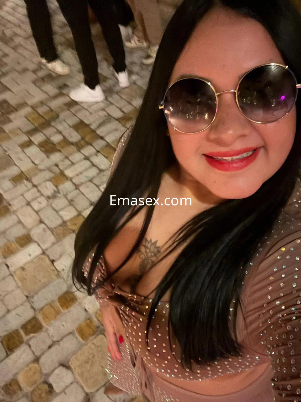Puta con cabello largo y lacio, usando un vestido brillante y gafas de sol, sonríe en una calle de Toledo.