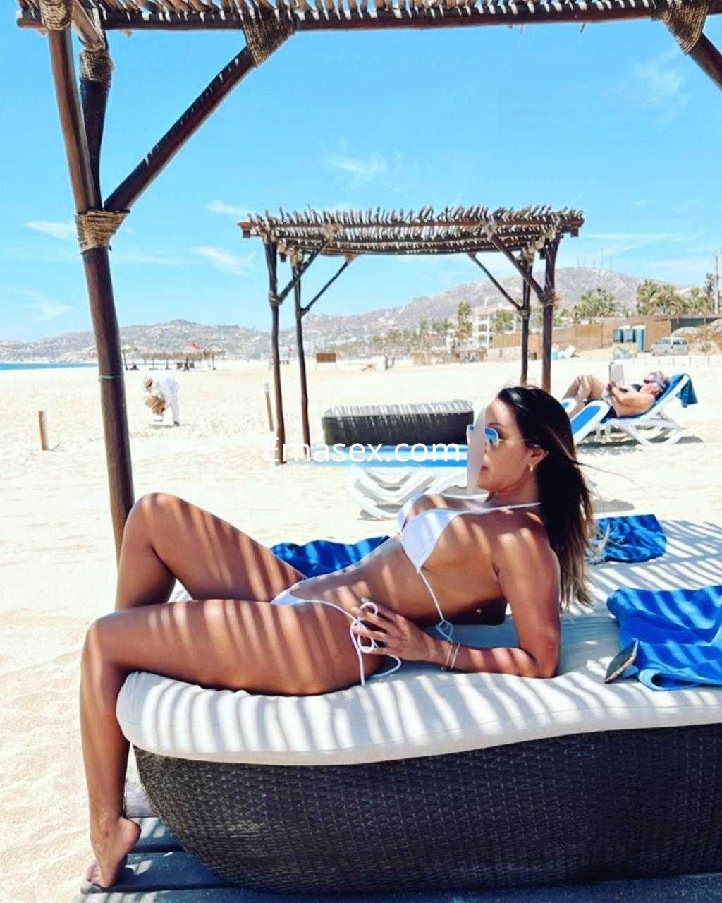 Escort en Málaga relajándose en una tumbona de playa, luciendo un bikini blanco y gafas de sol.