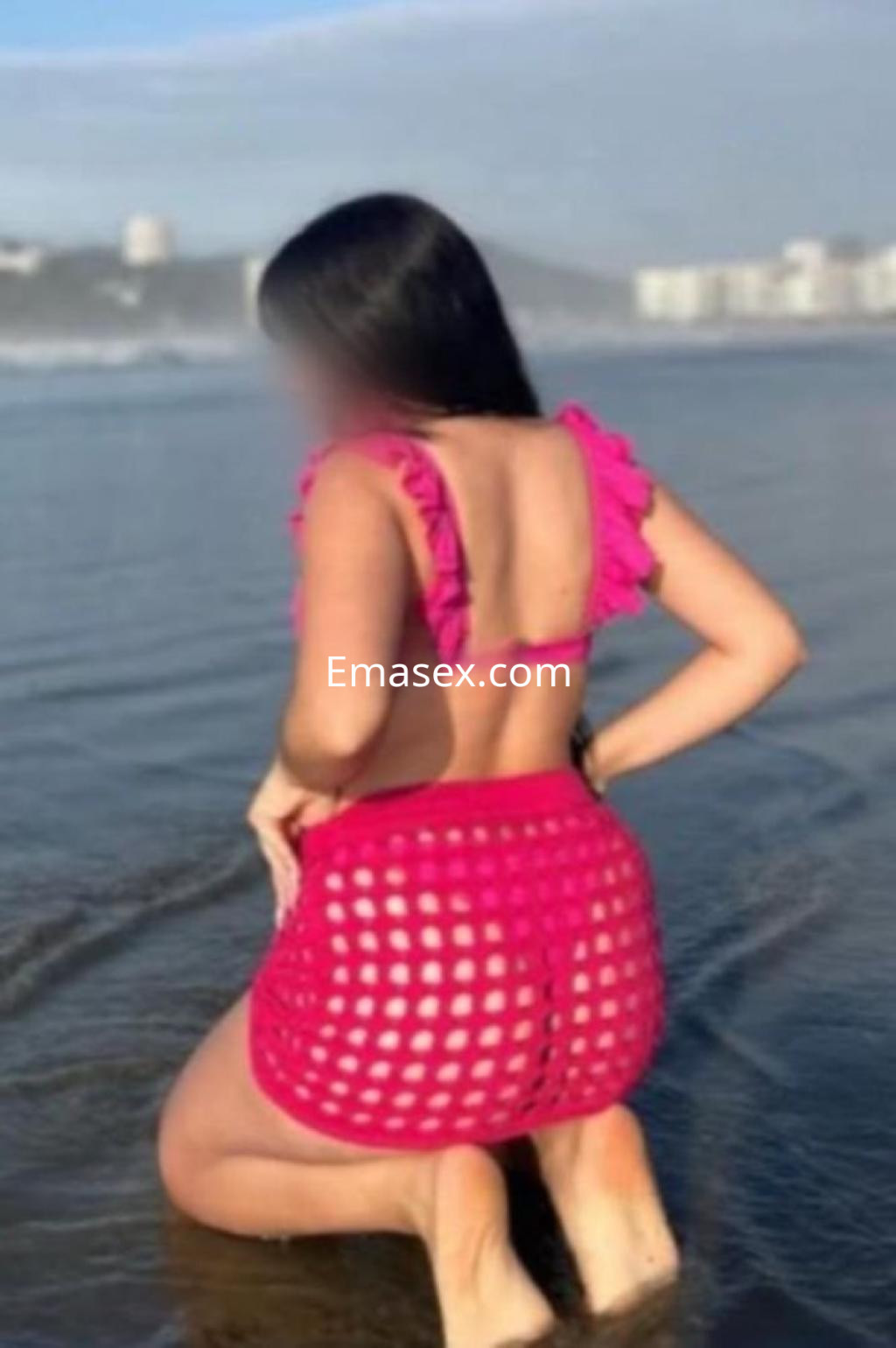 Escort en Lugo, de pie en la orilla del mar, viste un top rosa con volantes y una falda de red a juego.