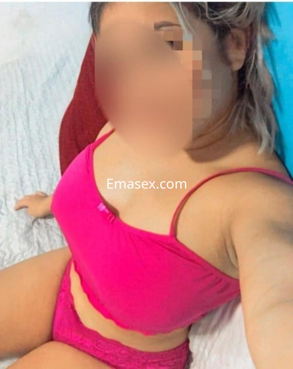 Escort en Ibiza, sentada en una cama, viste un conjunto de lencería rosa y tiene el cabello rubio.