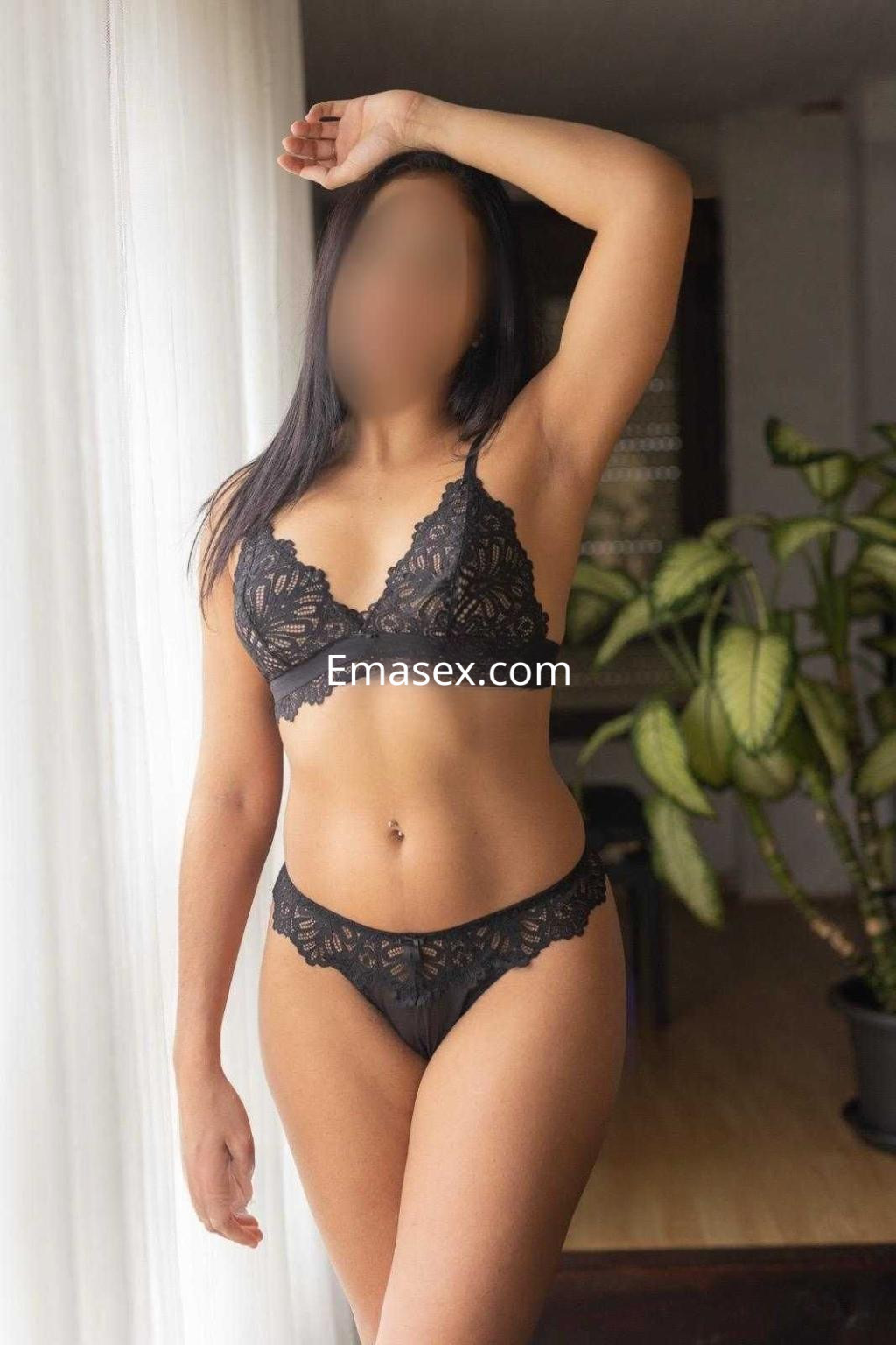 Puta en Cádiz luciendo un conjunto de lencería negra, de pie, con una mano en la cadera y cabello oscuro.