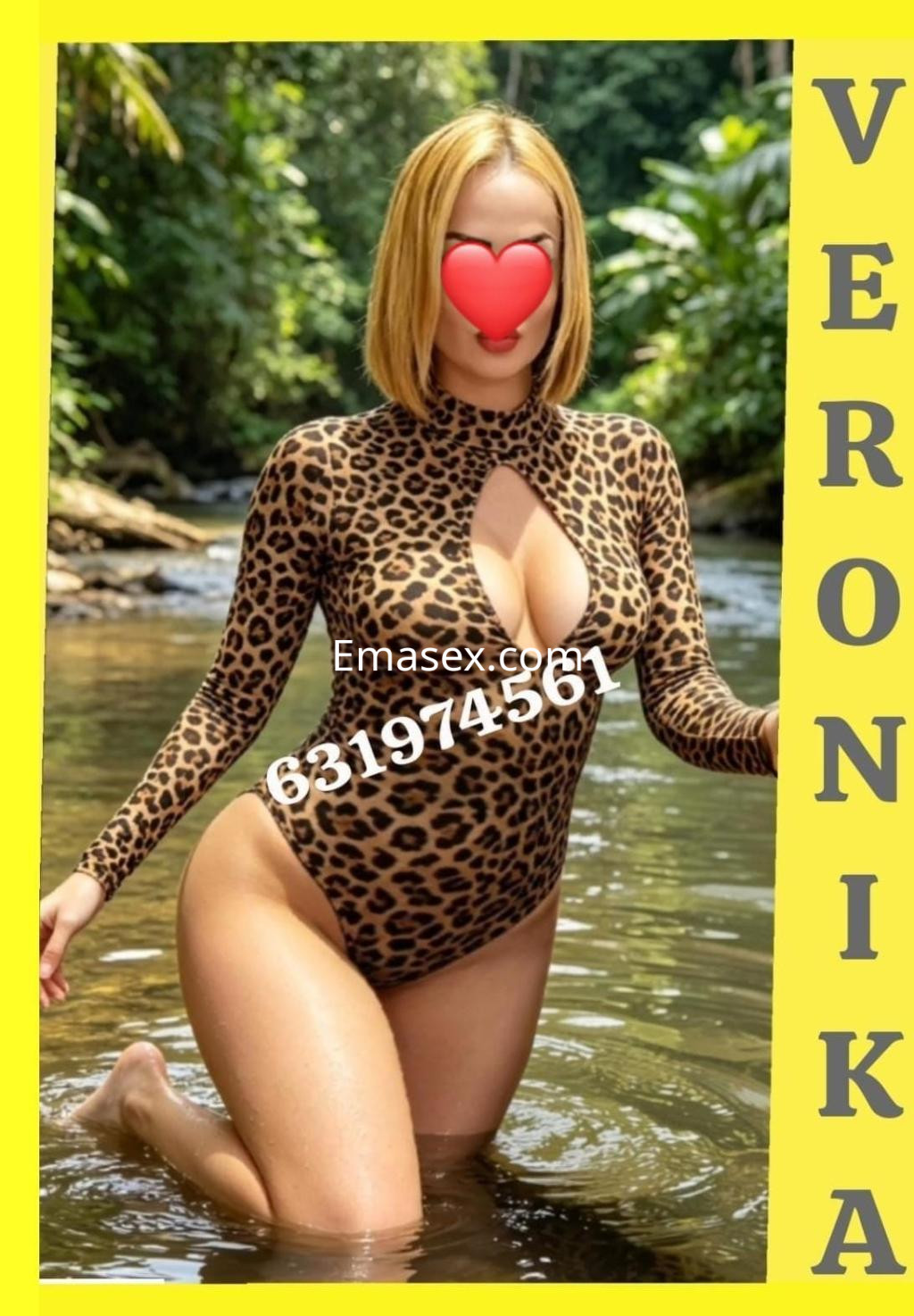 Escort en Alicante con cabello rubio, vistiendo un traje de baño de leopardo, posando en el agua rodeada de vegetación.