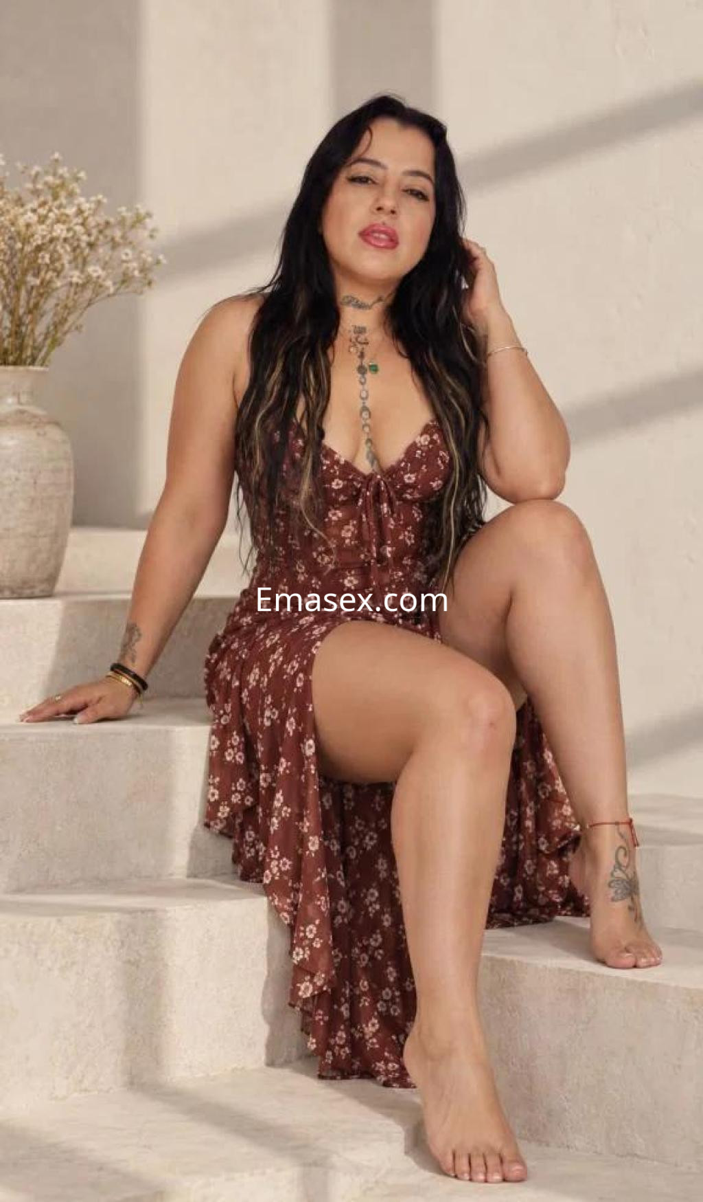 Escort en Toledo, sentada en escaleras con un vestido marrón de flores, mostrando una pose relajada y segura.