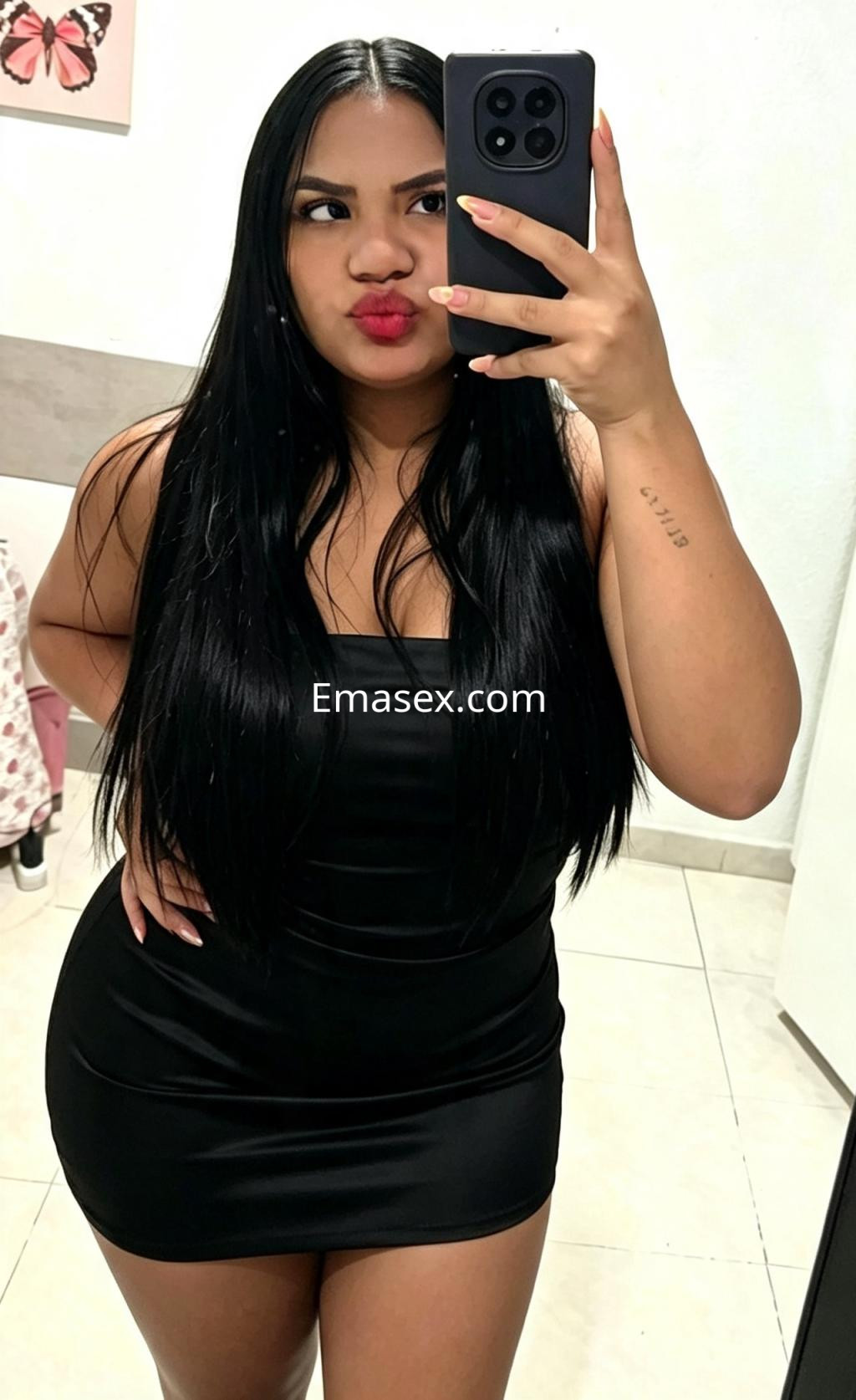La escort de Vigo se muestra en un espejo con un vestido negro ajustado, luciendo labios rojos y cabello largo.