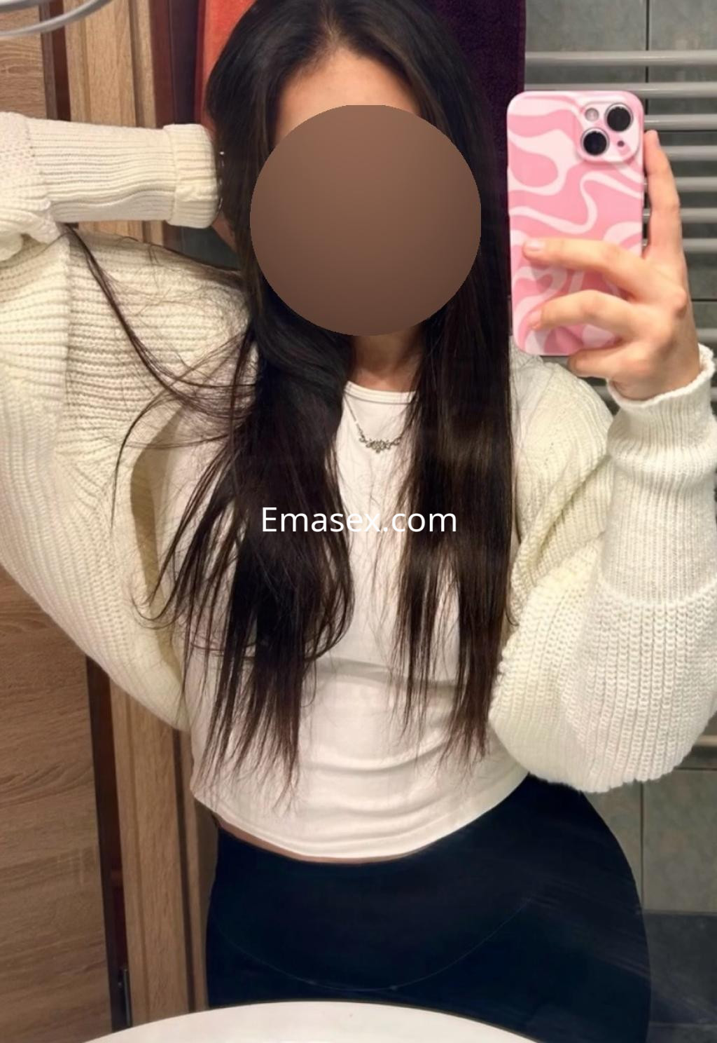 Puta de Pamplona con cabello largo y oscuro, viste un suéter blanco y una camiseta ajustada, posando frente al espejo.