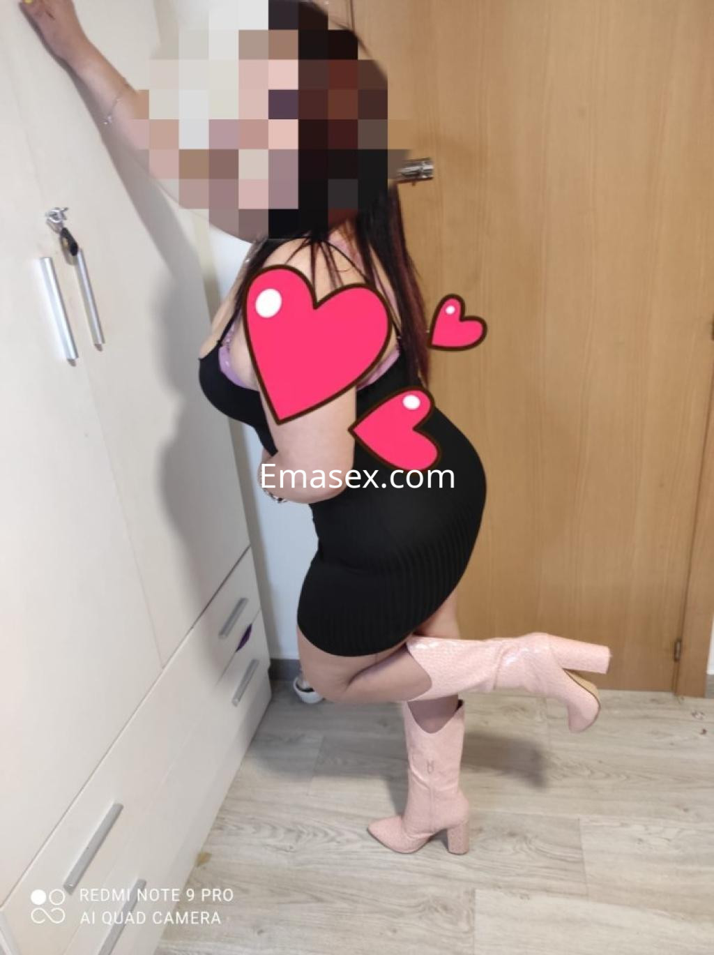 Escort con vestido negro ajustado y botas rosas, posando en un ambiente interior de Logroño.