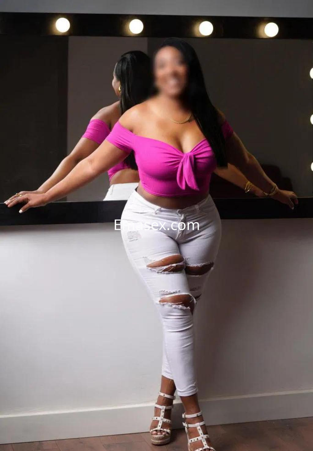 Escort en Tenerife con blusa rosa ajustada y pantalones blancos rasgados, posando frente a un espejo.
