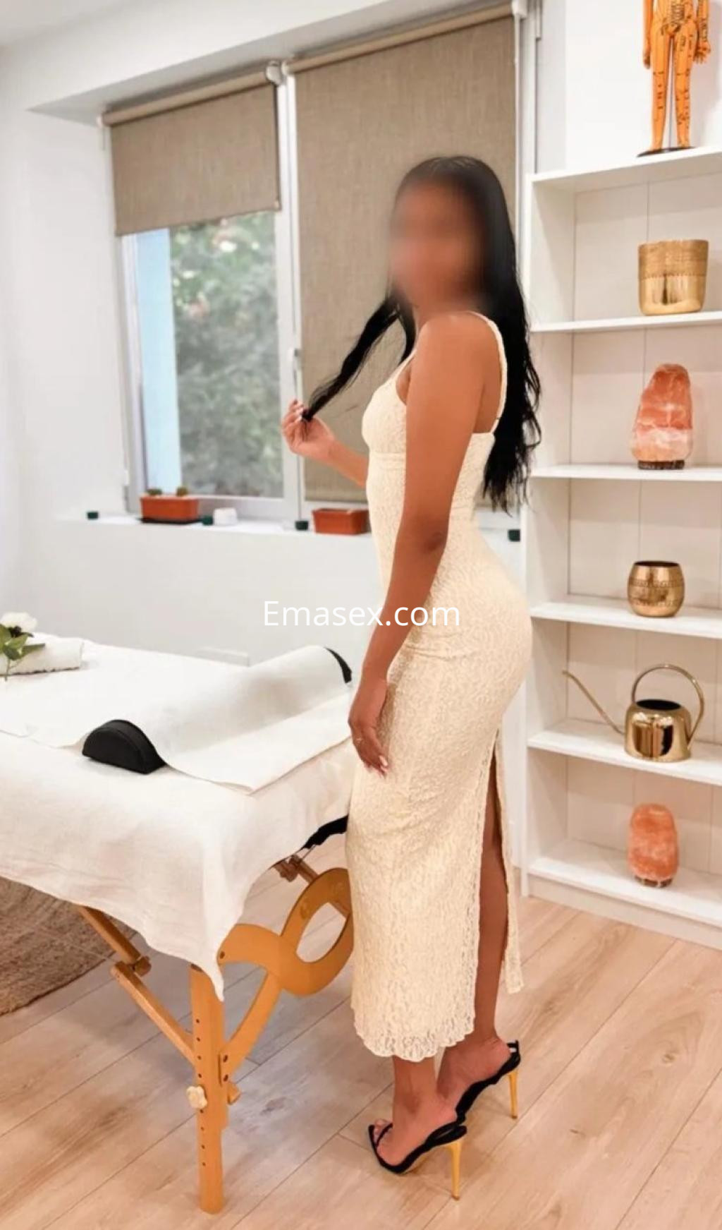 La puta se muestra de pie en un entorno acogedor de Palma de Mallorca, luciendo un vestido claro con abertura.