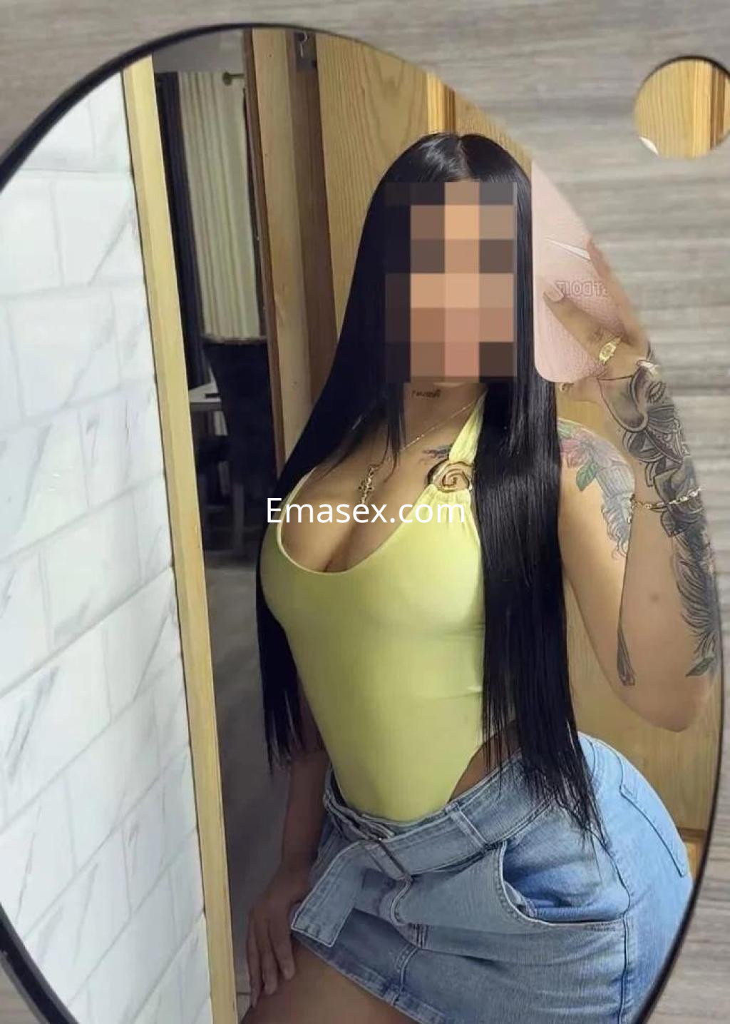 Escort en Tenerife con cabello largo y lacio, usando un body amarillo y una falda de mezclilla, posando frente a un espejo.