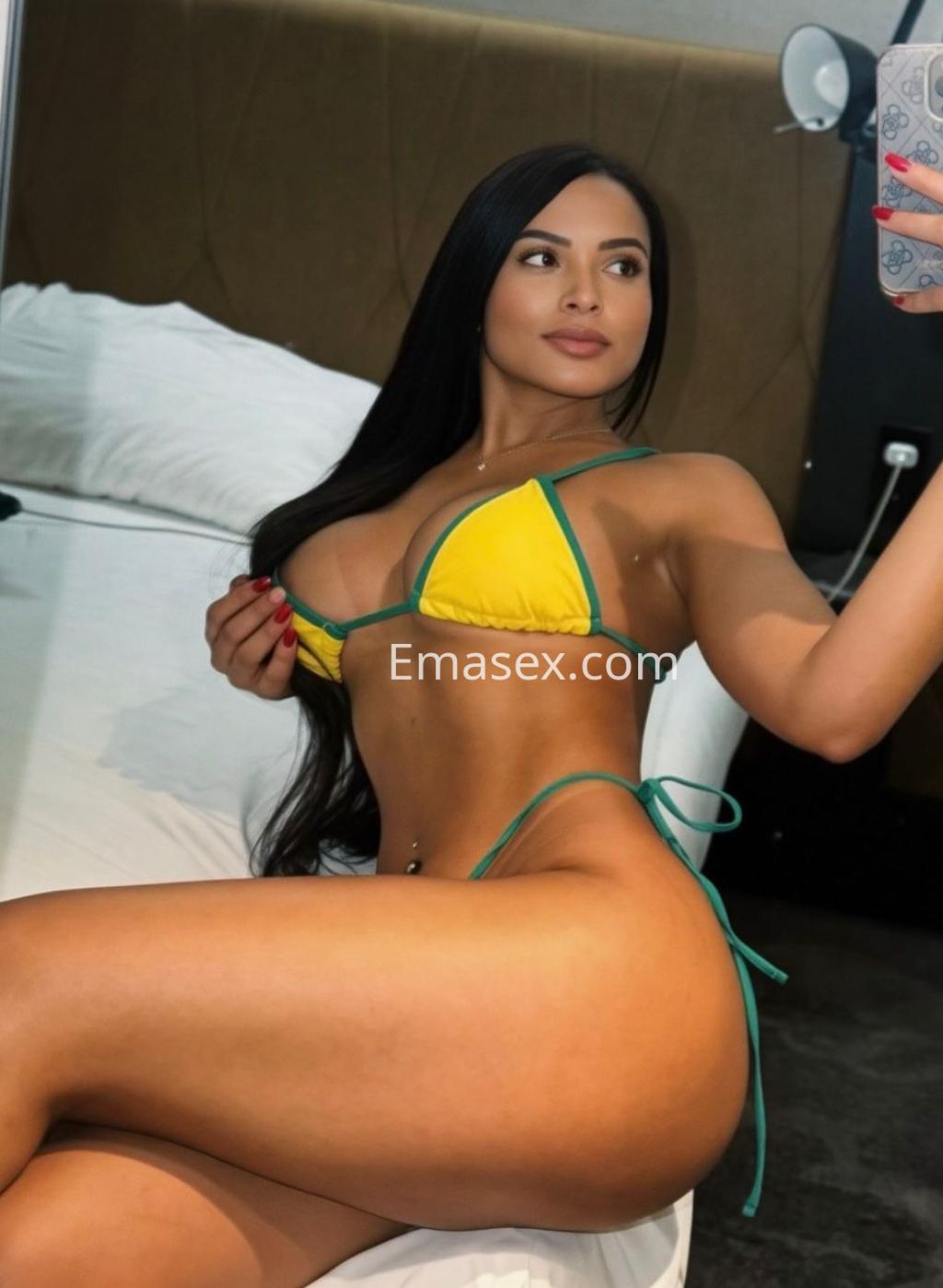 Escort en Málaga se fotografía en un espejo, vistiendo un bikini amarillo con tirantes verdes que destaca su figura.