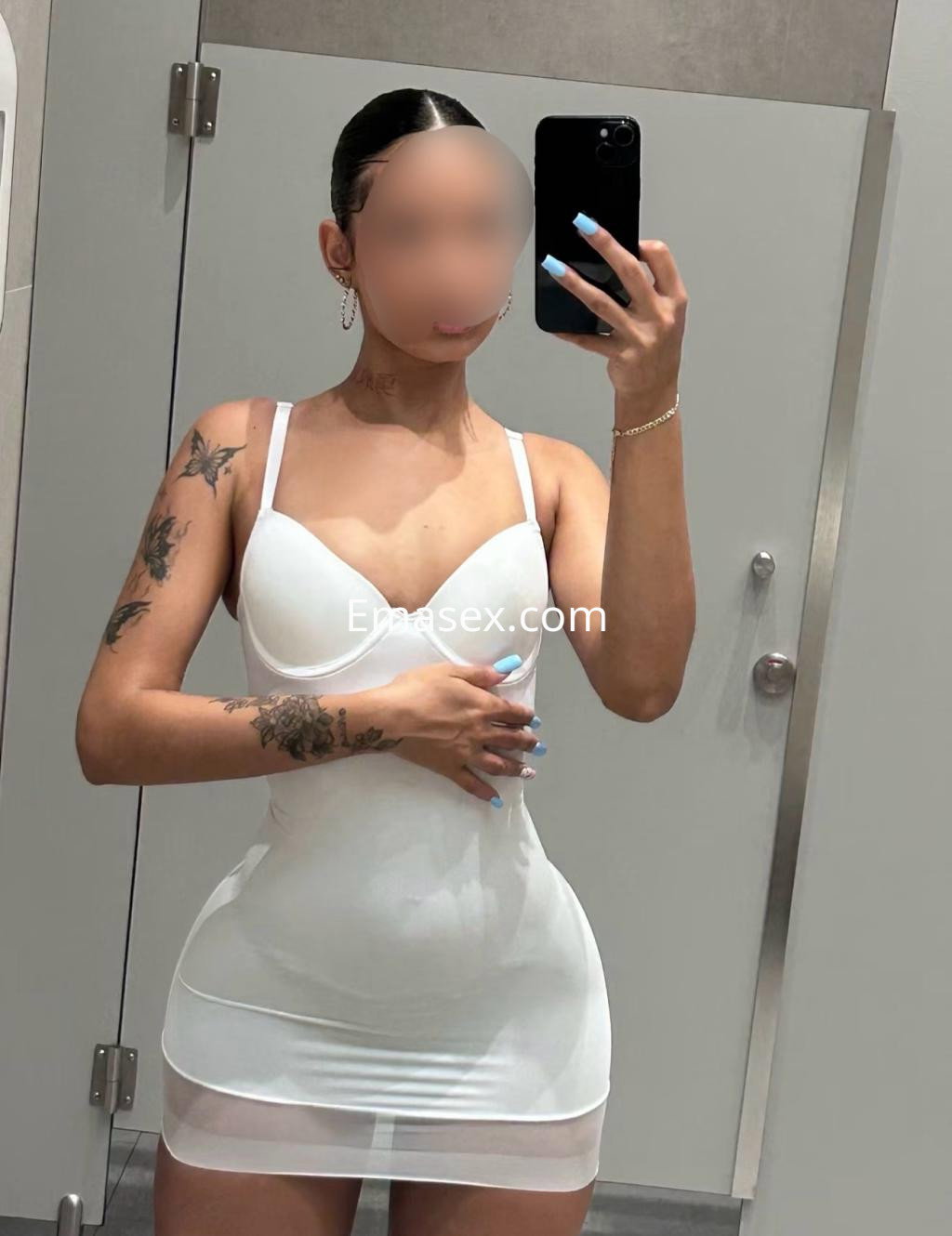 Escort en Vigo posando frente al espejo con un vestido blanco ajustado y detalles de tatuajes visibles.