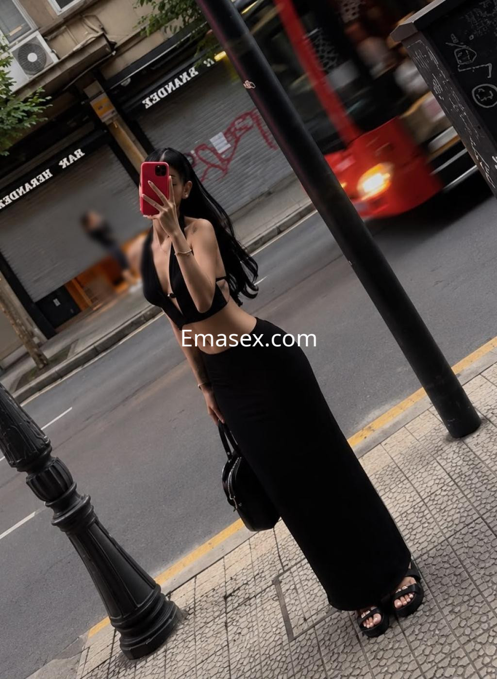 Escort en Bilbao luciendo un top negro y una falda larga, posando en la calle con un bolso y cabello lacio.