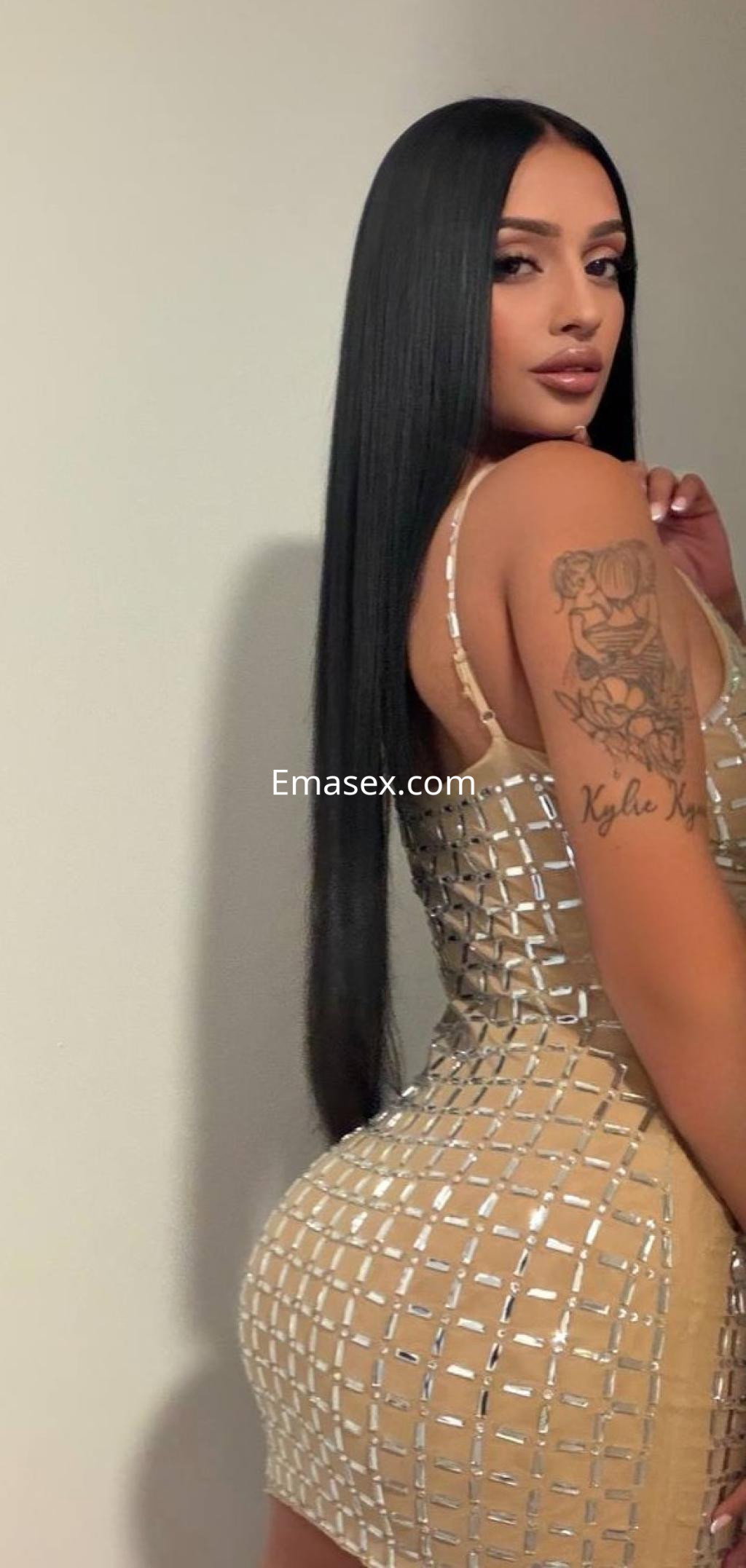 Escort en Donosti viste un vestido ajustado de color dorado con detalles metálicos, mostrando su cabello lacio.