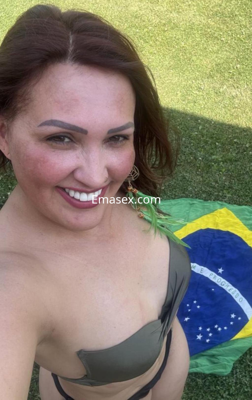 Puta en Coruña posando con una gran sonrisa, vistiendo un bikini verde, sobre una bandera de Brasil.