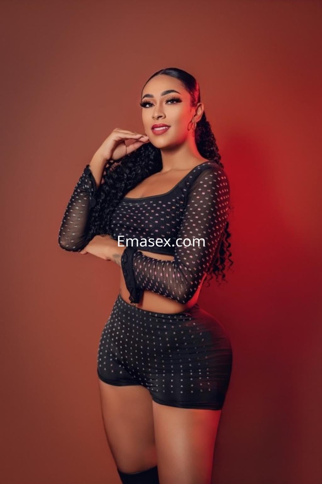 Escort en Santander con cabello rizado y largo, viste un conjunto negro con detalles brillantes que resalta su figura.