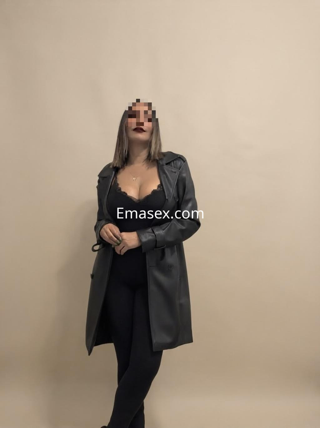 Puta en Madrid, con cabello lacio y oscuro, viste un abrigo negro sobre lencería en un fondo claro.