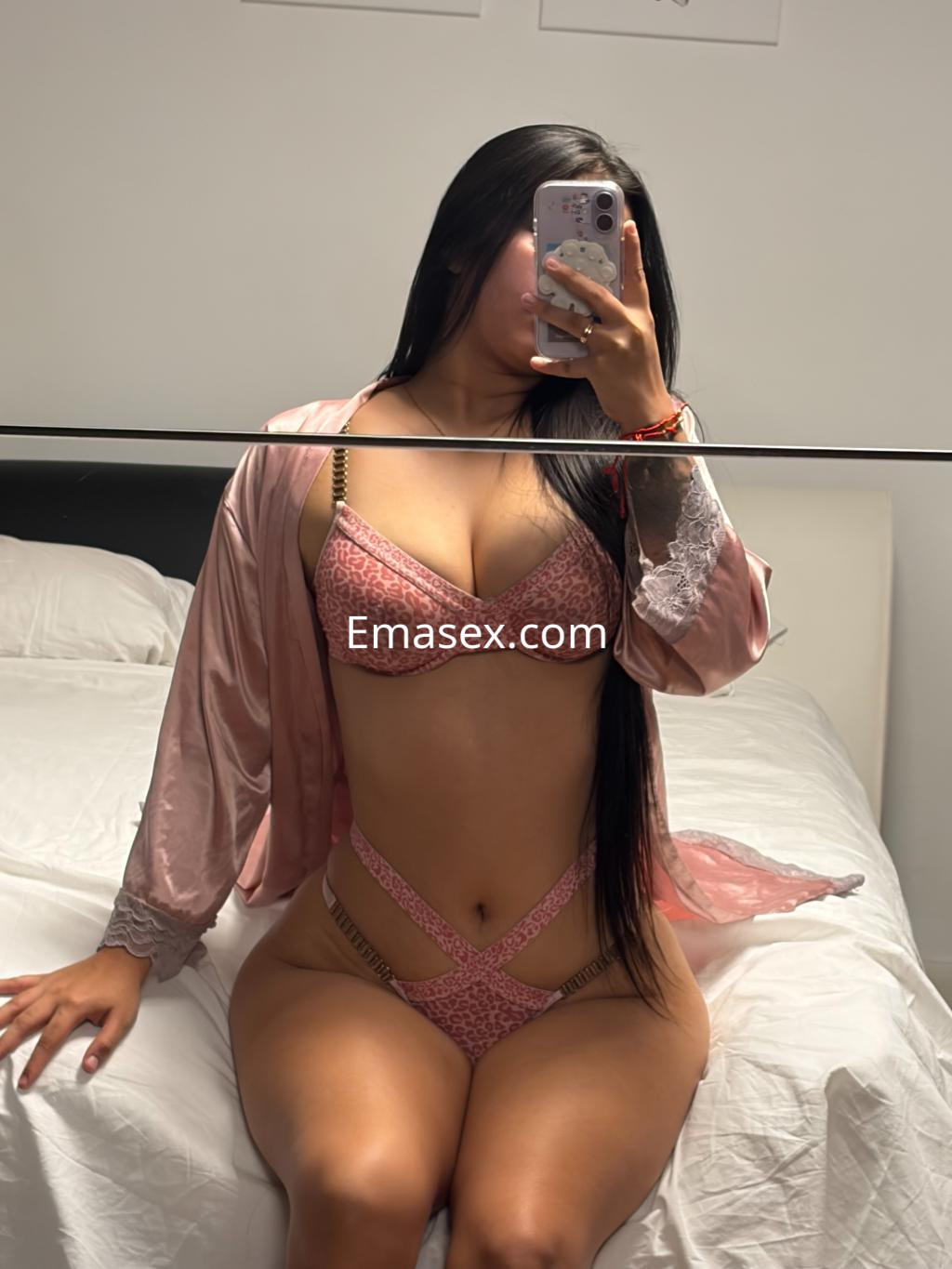 La puta en Logroño posa frente al espejo con lencería rosa y un kimono suave, mostrando su figura.