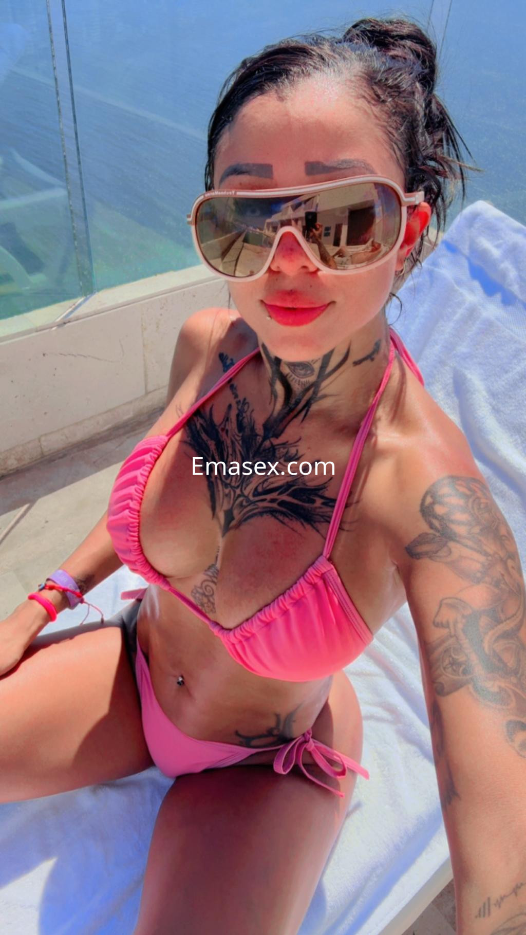 Puta con bikini rosa y gafas de sol, posando en una tumbona con vista al mar en Madrid.