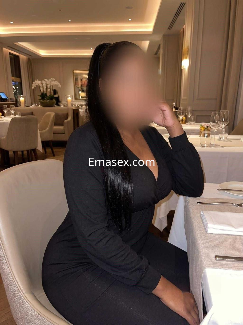 Puta sentada en un elegante restaurante de Tenerife, luciendo un atuendo negro ajustado y peinado con coleta.