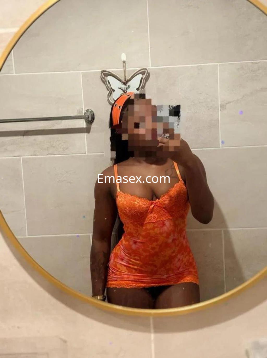 La puta posa frente a un espejo, luciendo una lencería naranja ajustada en un baño de Girona.