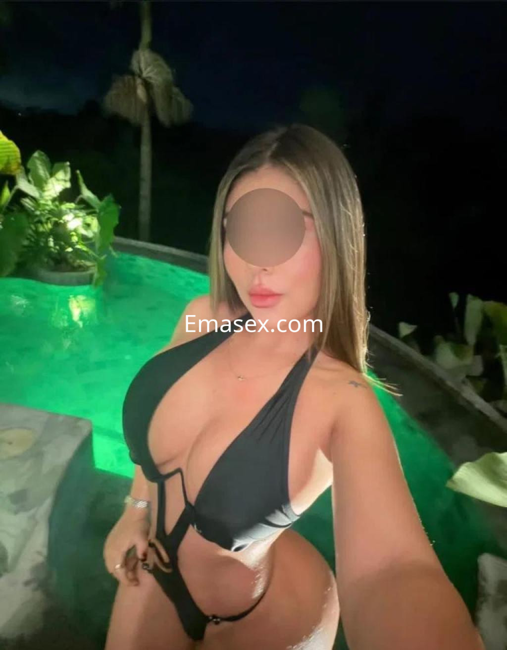 Escort en Tenerife posando frente a una piscina iluminada, luciendo un traje de baño negro con detalles en la cintura.