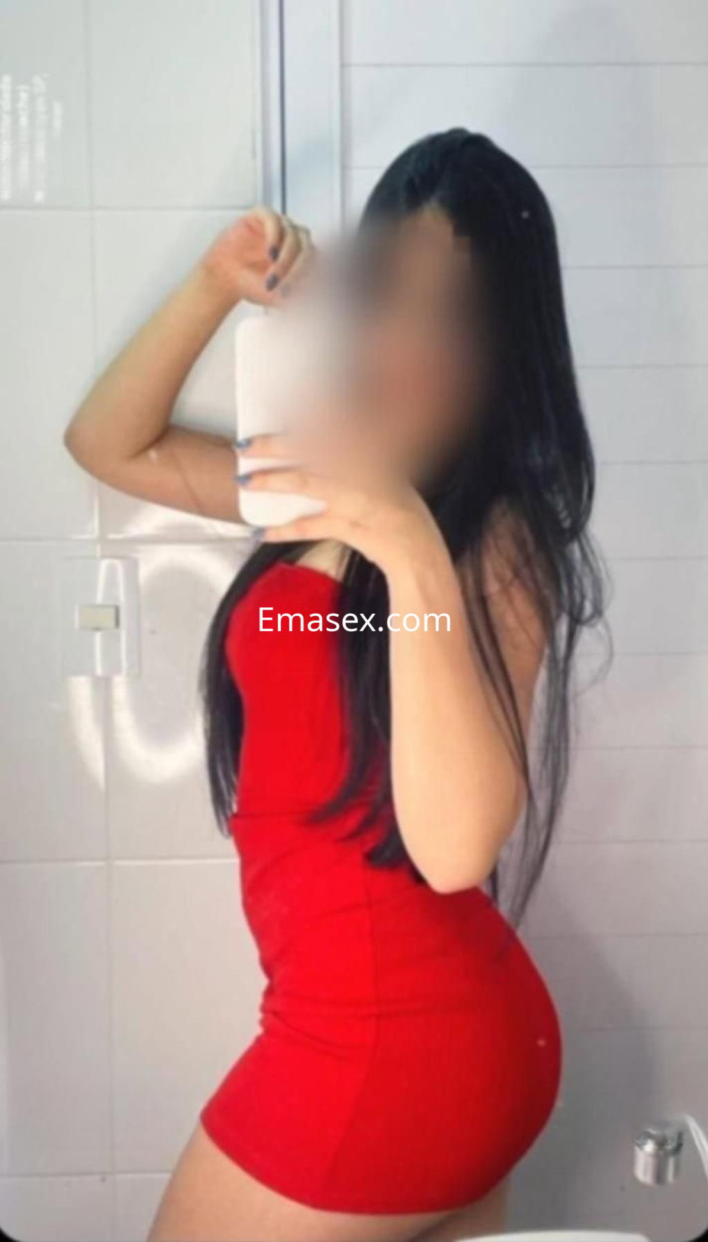 Puta en Badajoz, posando frente a un espejo, luciendo un vestido rojo ajustado y con el cabello largo.