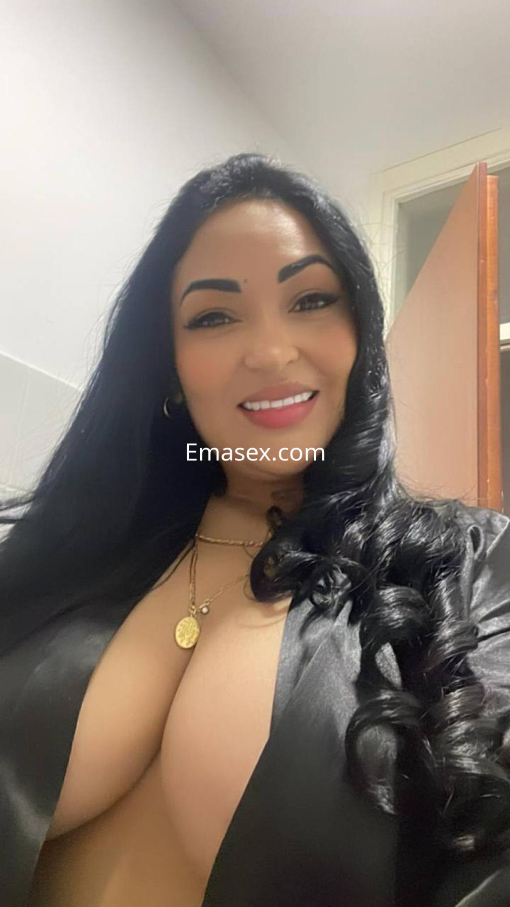 Escort en Donosti con cabello largo y rizado, vistiendo una blusa negra que acentúa su figura y sonriendo.