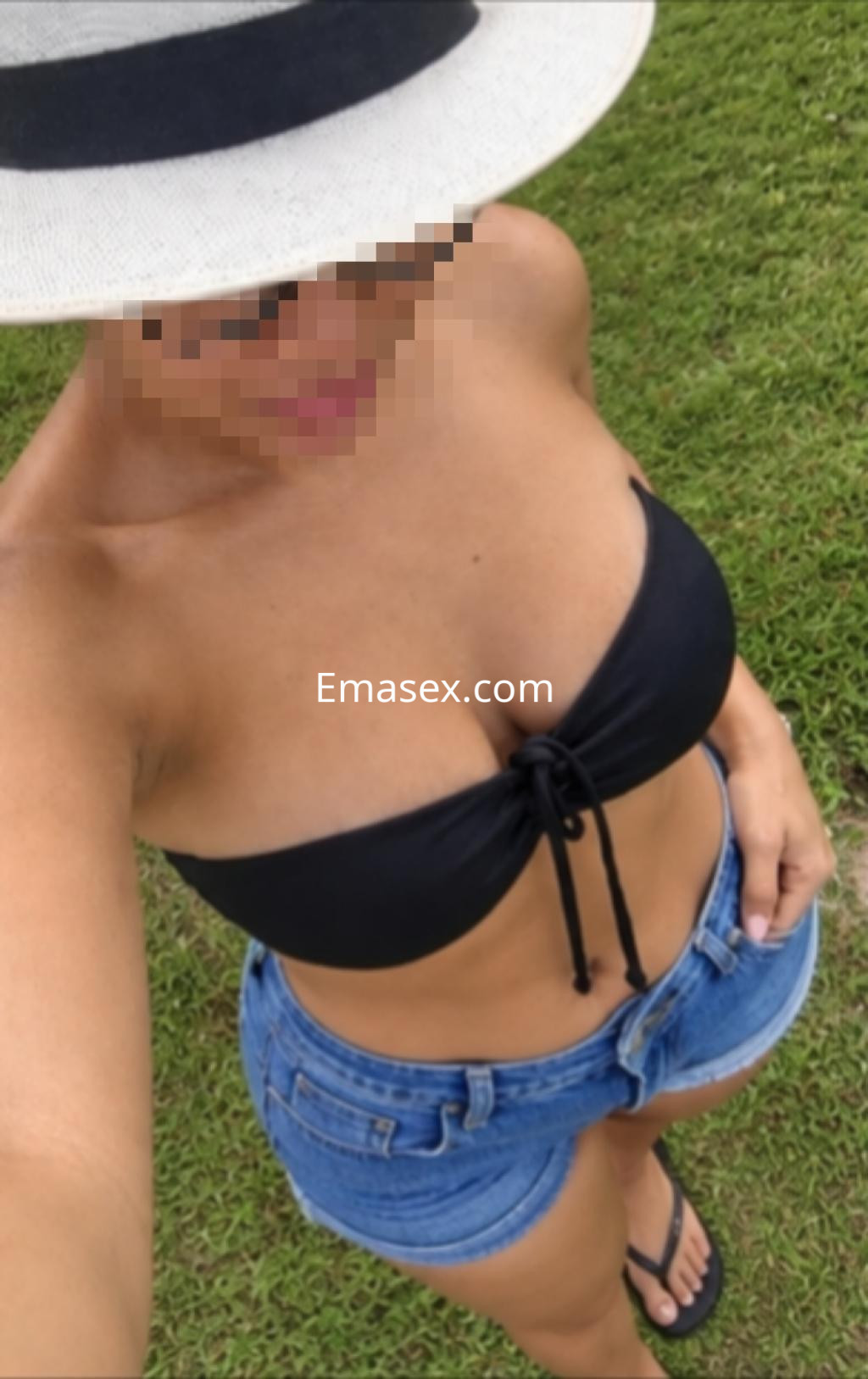 Escort de Pamplona con cabello lacio, lleva un bikini negro y shorts de mezclilla, posando en un entorno verde.