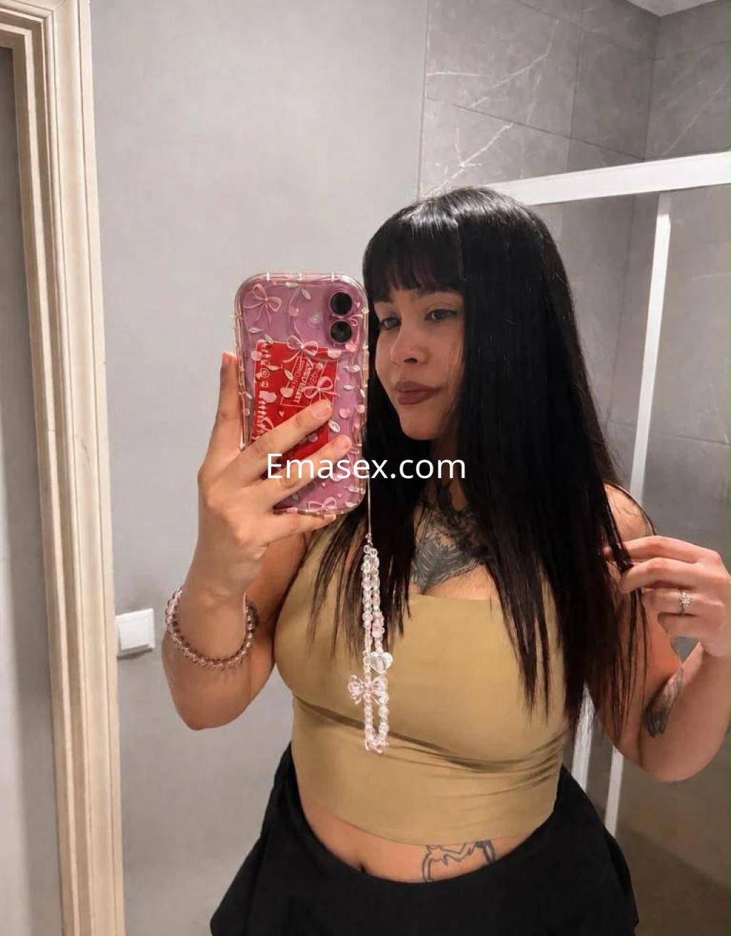 Escort en Girona con cabello largo y lacio, viste una blusa ajustada color beige y muestra un tatuaje en el brazo.