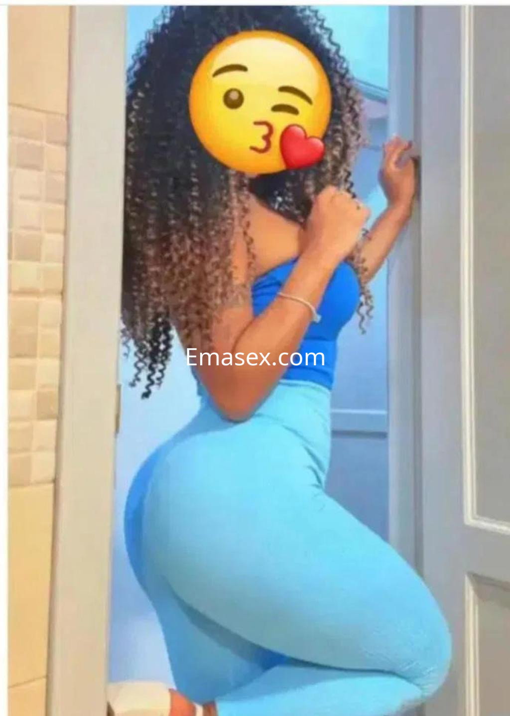 Puta con cabello rizado, vistiendo un conjunto azul ajustado, posando en una puerta en Córdoba.