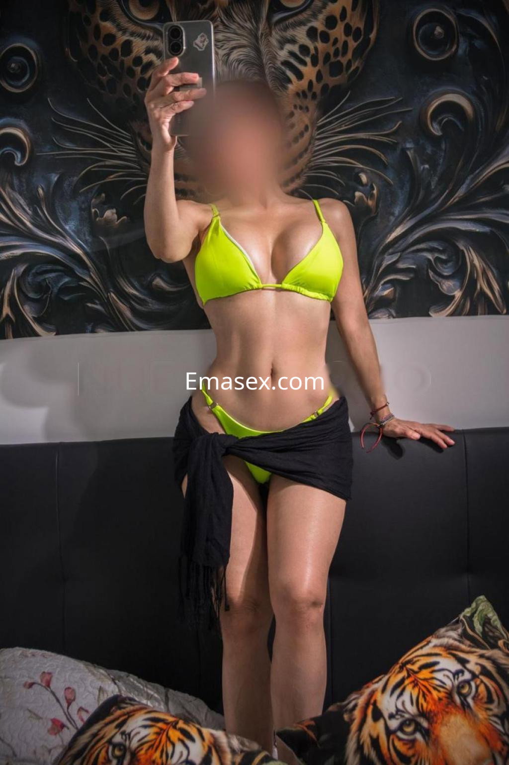 Escort en Barcelona posando con un bikini amarillo neón y una prenda negra alrededor de la cintura, en un ambiente decorado.