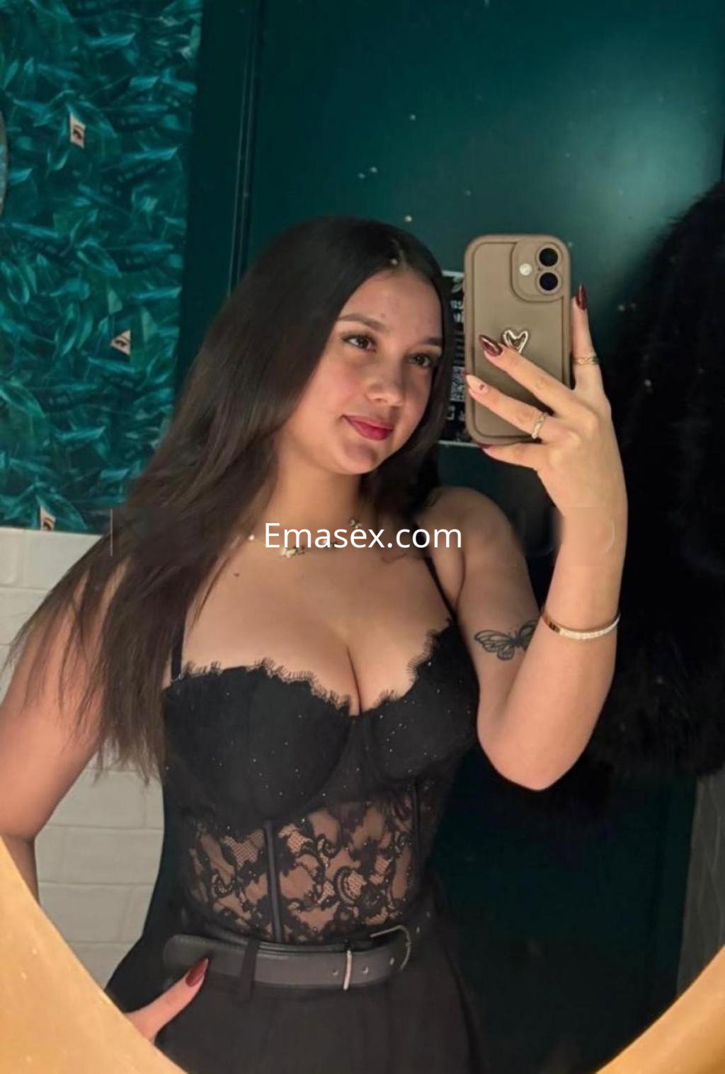 Escort en Barcelona posando frente al espejo, luciendo un conjunto negro con detalles de encaje y cabello largo.