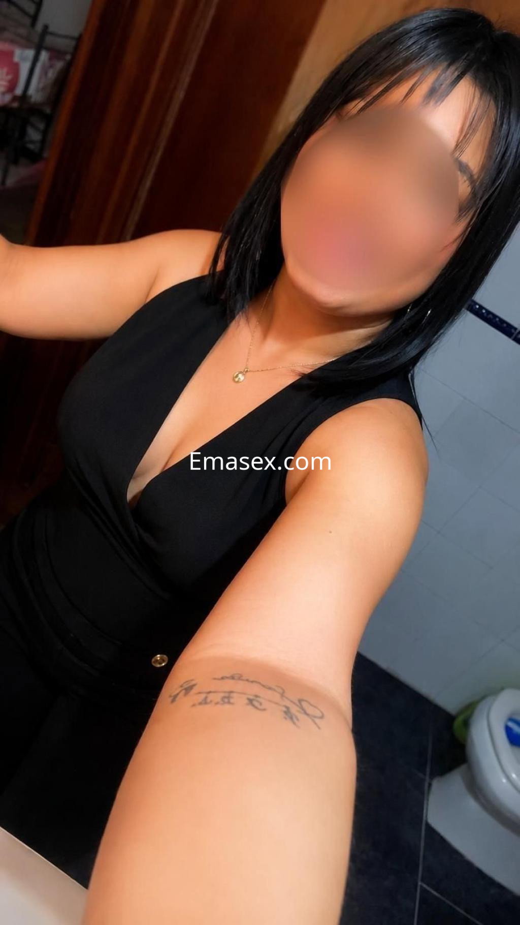 Escort en Sevilla, luciendo un vestido negro ajustado y posando frente a un espejo en un baño moderno.