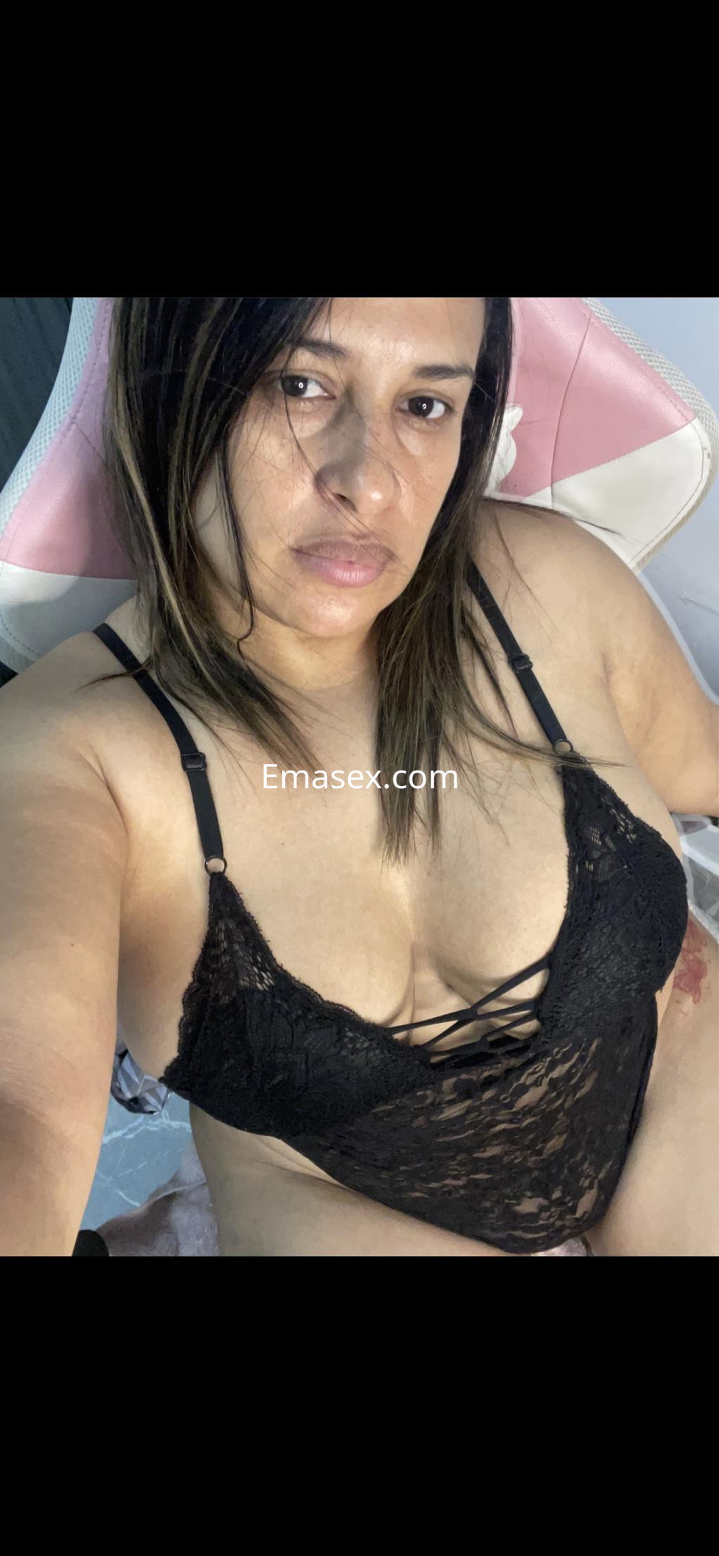 Escort en Irún, con cabello castaño y lacio, luciendo un body de encaje negro mientras se toma una selfie.