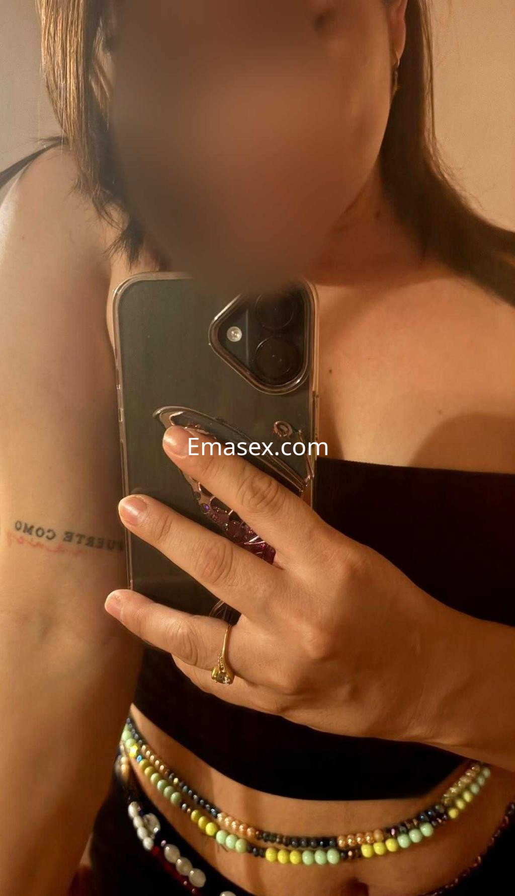 La escort en Almería se presenta con un top negro, mostrando un tatuaje en el brazo y un collar de cuentas coloridas.