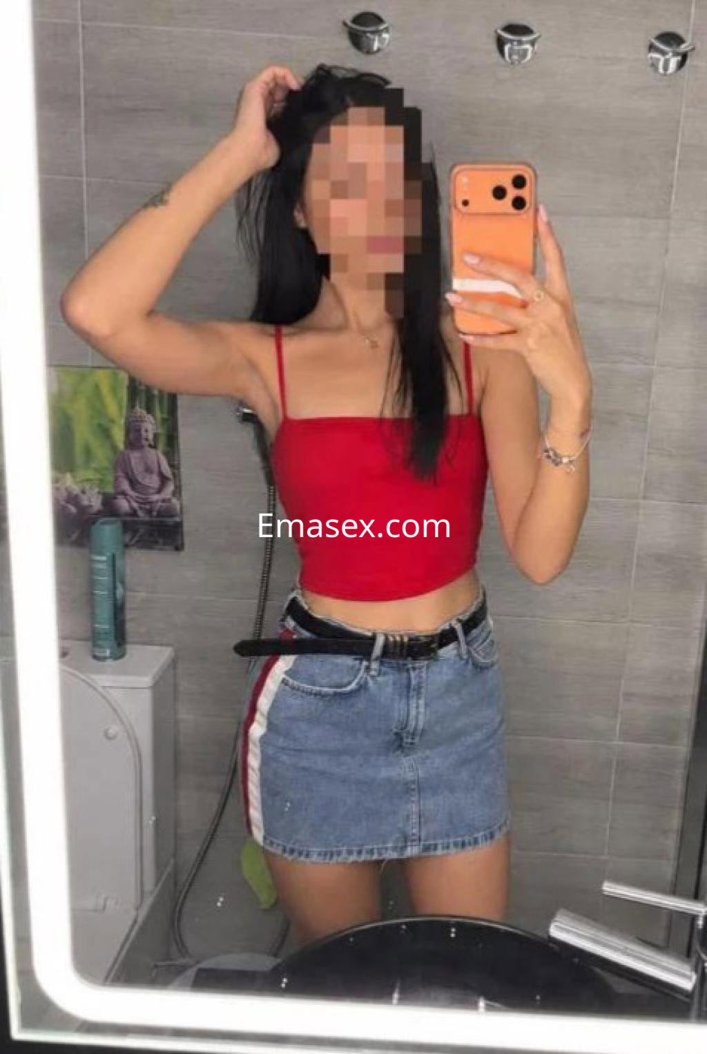 Puta en Madrid se toma un selfie en el baño, luciendo un top rojo y una falda de mezclilla corta.