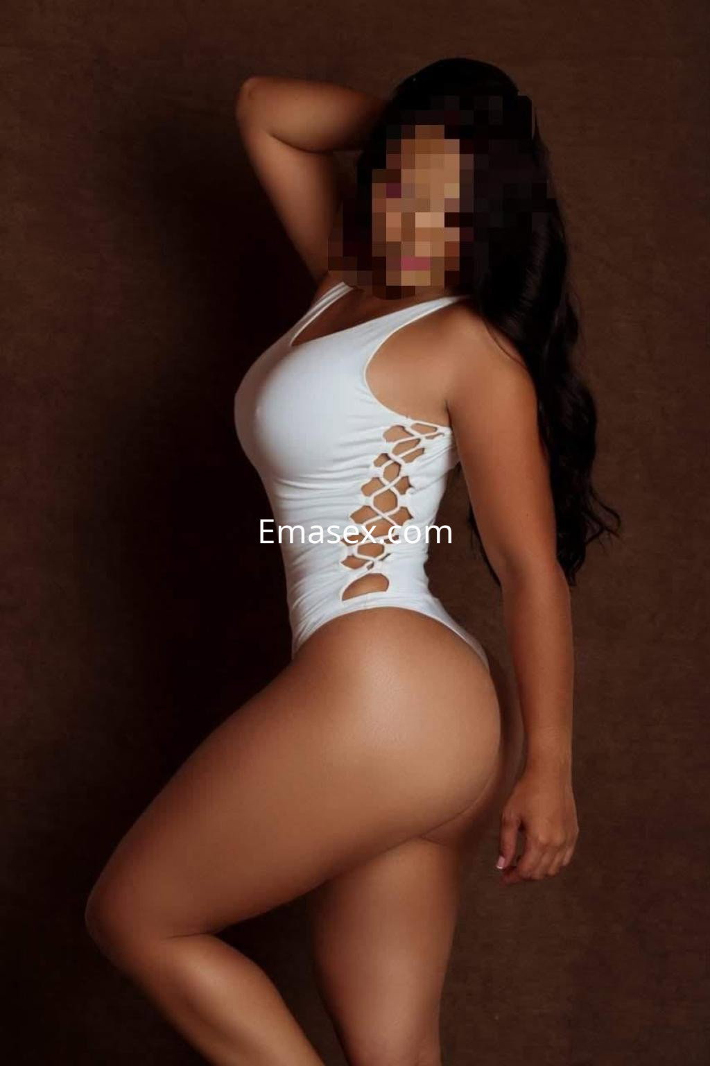 Escort en Donosti posando de perfil con un traje de baño blanco que destaca su figura y cabello largo.