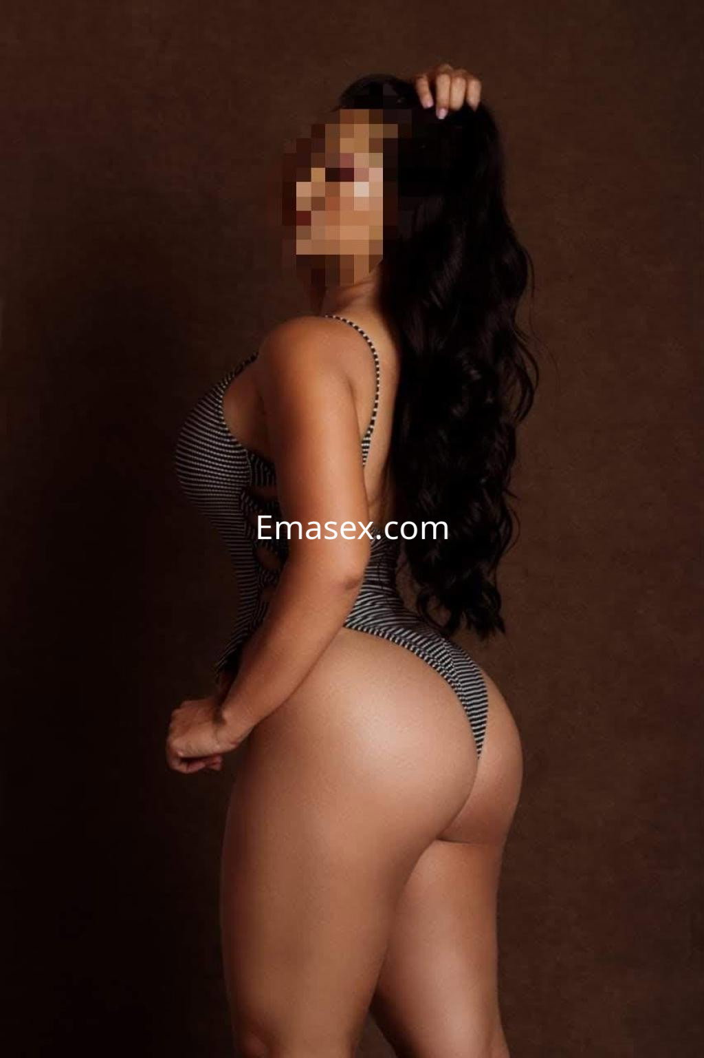 La escort de Irún posa de perfil en un traje de baño de rayas, con cabello largo y ondulado.