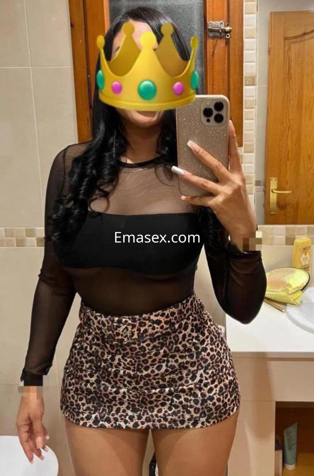 Escort en Las Palmas lleva una blusa negra transparente y una falda corta de leopardo, posando frente al espejo.