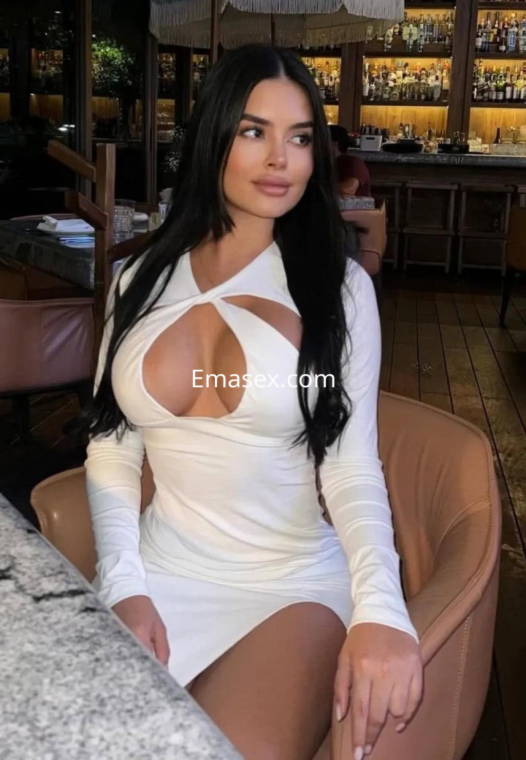 Puta en Coruña, con cabello largo y lacio, viste un vestido blanco ajustado con cortes y se encuentra sentada en un bar.